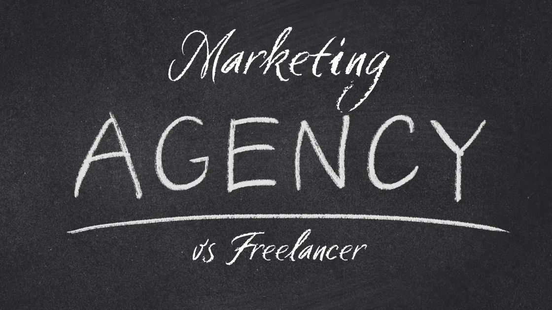 Chalkboard sign reading Marketing Agency vs Freelancer